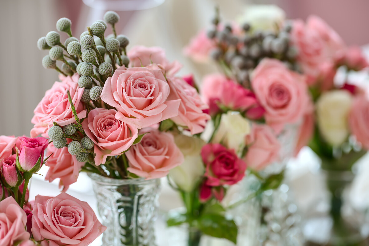 Mazzolini di rose rosa e fucsia con bacche grigie di brunia in vasetti di vetro lavorato su un tavolo chiaro